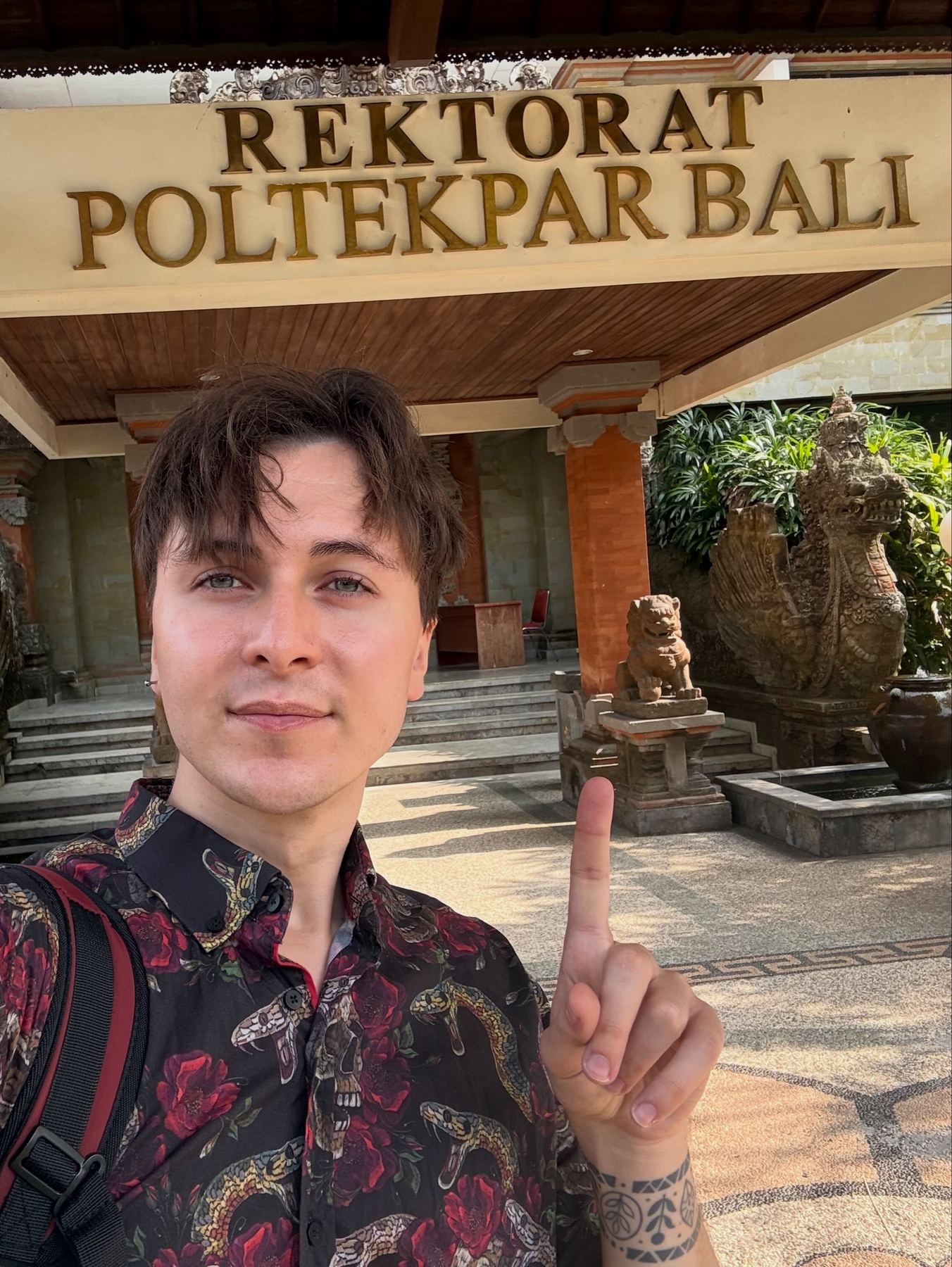 Maciej pointing up at the Rektorat Poltekpar Bali sign